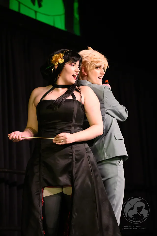 Two performers in Spy x Family cosplay (Yor and Loid Forger) posing together on stage.