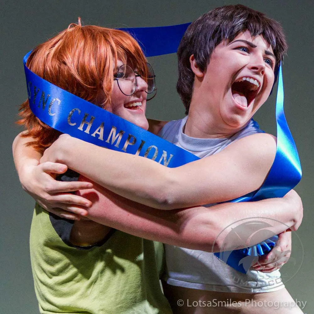 Two winners of the 2017 Lip Sync Showdown hugging joyfully while wearing a blue "Champion" sash.