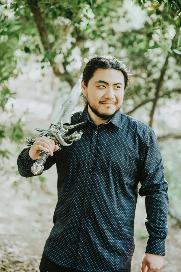 Portrait of Kaiji Tang holding a large fantasy sword.