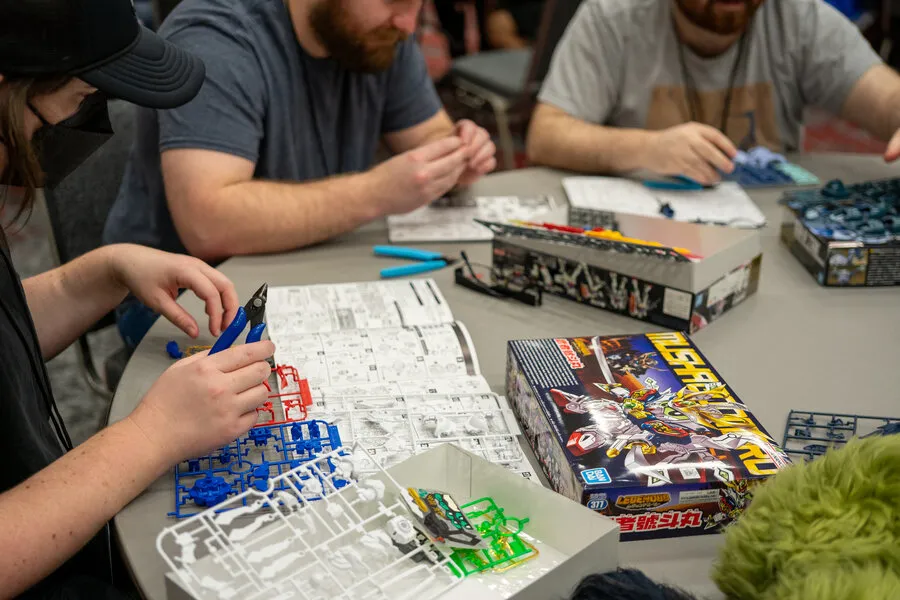 People sitting at a table carefully assembling Gundam model kits using nippers and instruction manuals.