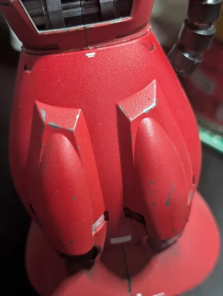 Close-up of weathered mechanical parts on a red model kit, showing realistic paint chipping and wear.