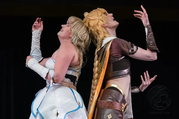 Two performers in Genshin Impact cosplay (Lumine and Aether) posing back-to-back.