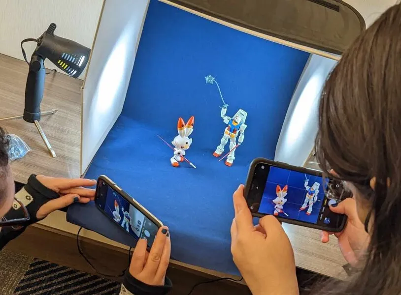A Gunpla photography setup with a blue backdrop and lights being used to photograph small figures.