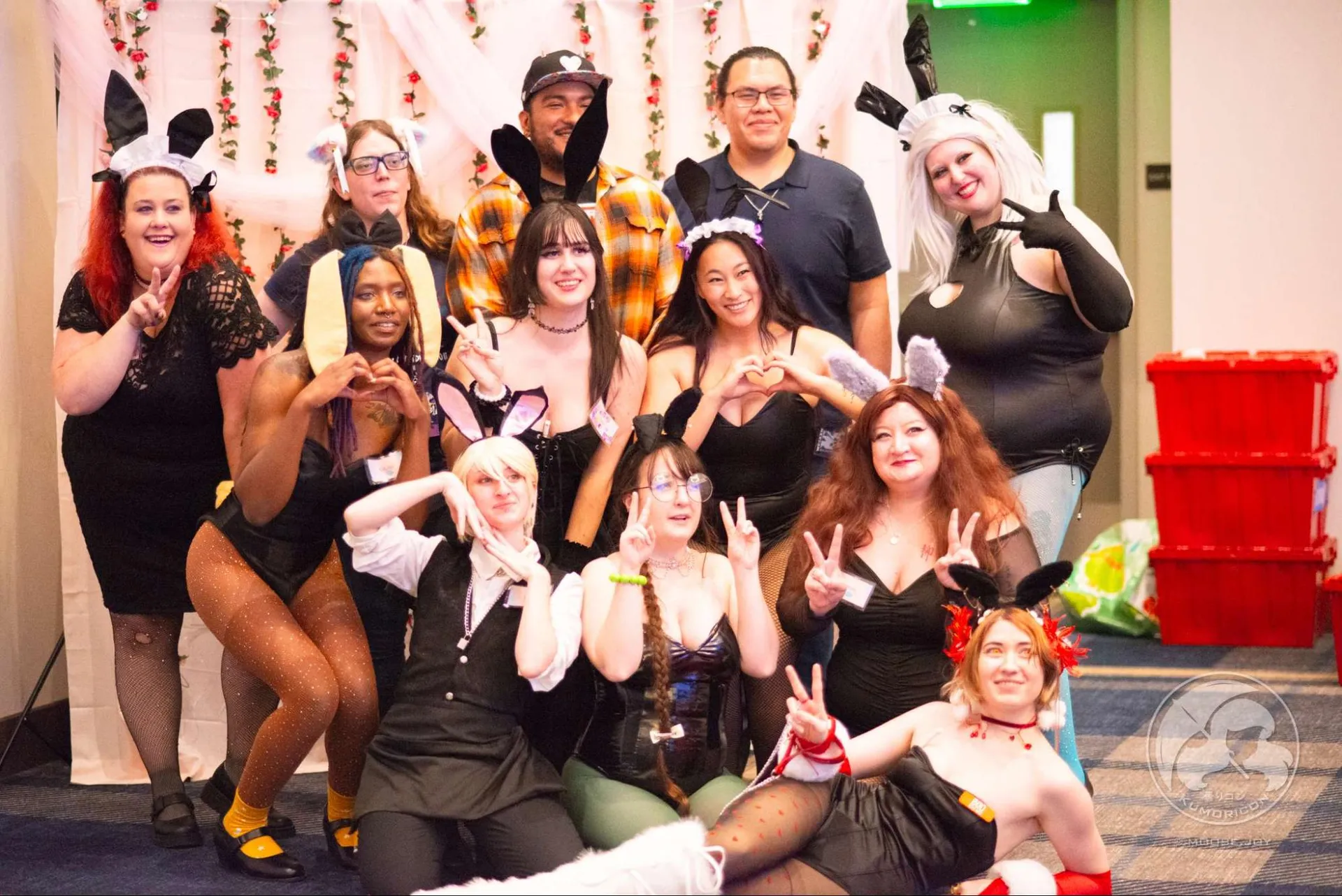 A large group of maid cafe staff in various cosplay and maid outfits posing together.