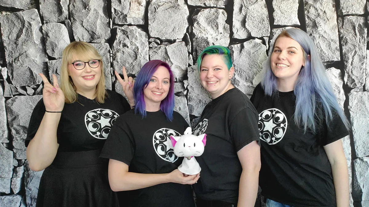 A group of four women smiling and posing in front of a stone wall background.