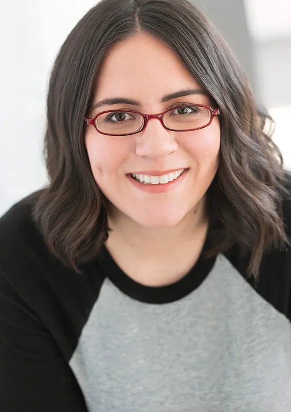 Portrait of Erica Mendez smiling, wearing glasses and a grey t-shirt.