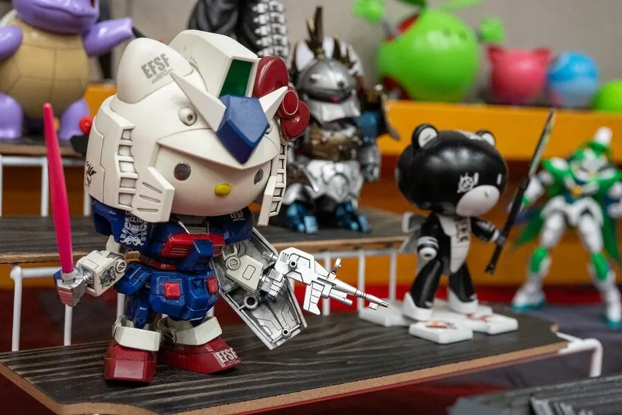 A variety of built Gunpla and anime figures, including a Hello Kitty Gundam, displayed on tiered shelving.