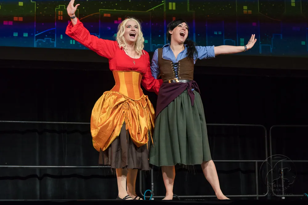 Two performers in historical or fantasy dresses singing passionately on stage.