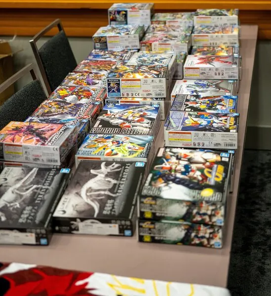 A long table filled with many unopened Gunpla and model kit boxes for a "Build-and-Take" event.
