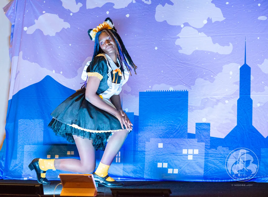 A maid cafe performer in a black and white maid outfit with animal ears posing on stage.