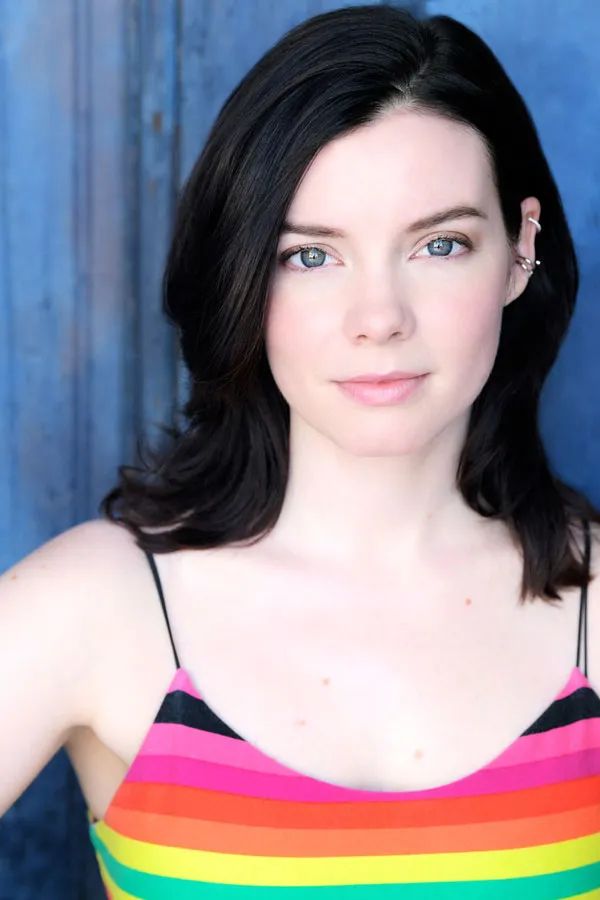 Portrait of Cherami Leigh in a rainbow-striped top against a blue background.