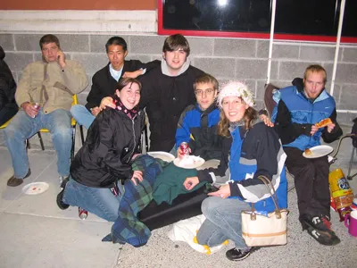 A group of friends posing outside a store with pizza and drinks while waiting in line at night.