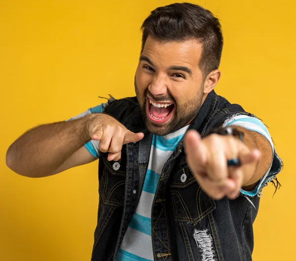 Portrait of Caleb Hyles smiling and pointing towards the camera, wearing a denim vest.