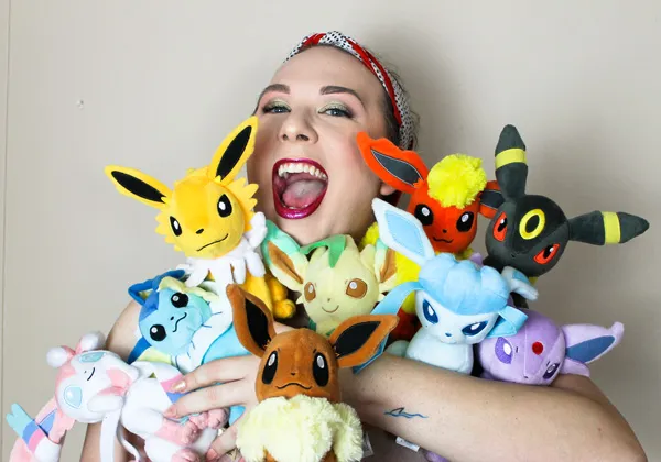 Portrait of Queen D smiling while holding several Eevee evolution plushies.