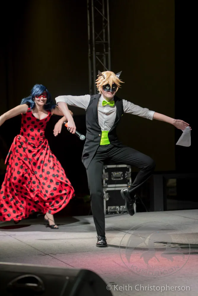 Two performers in Miraculous Ladybug cosplay (Ladybug and Cat Noir) dancing on stage.